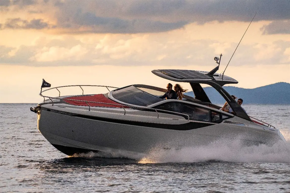 A sleek motorboat speeds over water at sunset, with passengers enjoying the ride on a stylish deck.